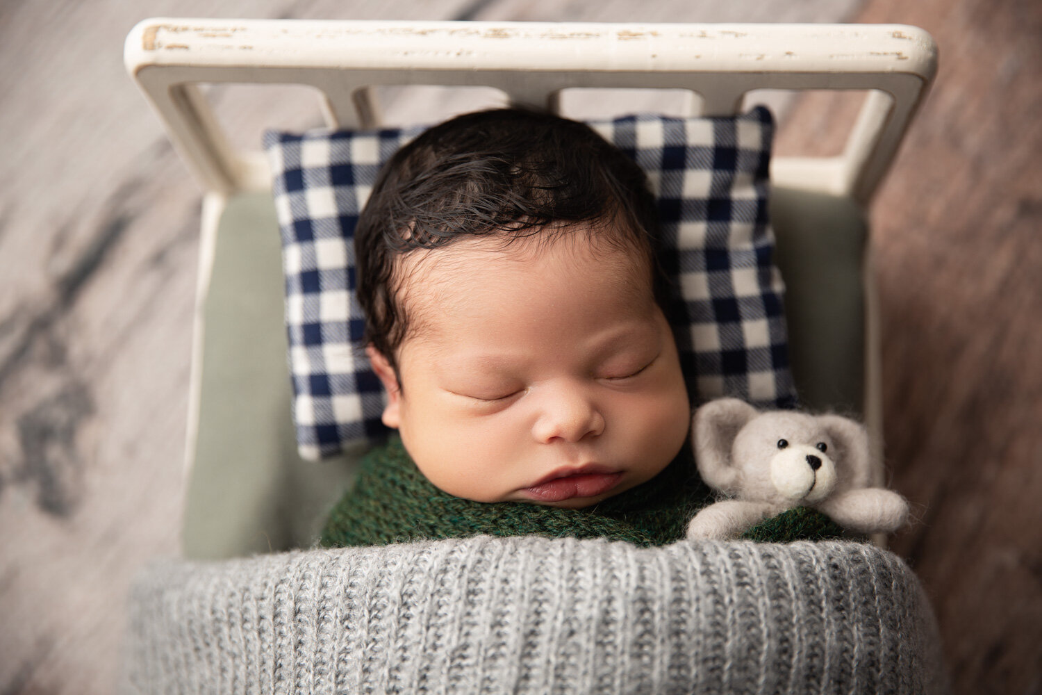  Dark haired newborn boy wrapped in green with grey blanket in bed prop during Winnipeg newborn session 