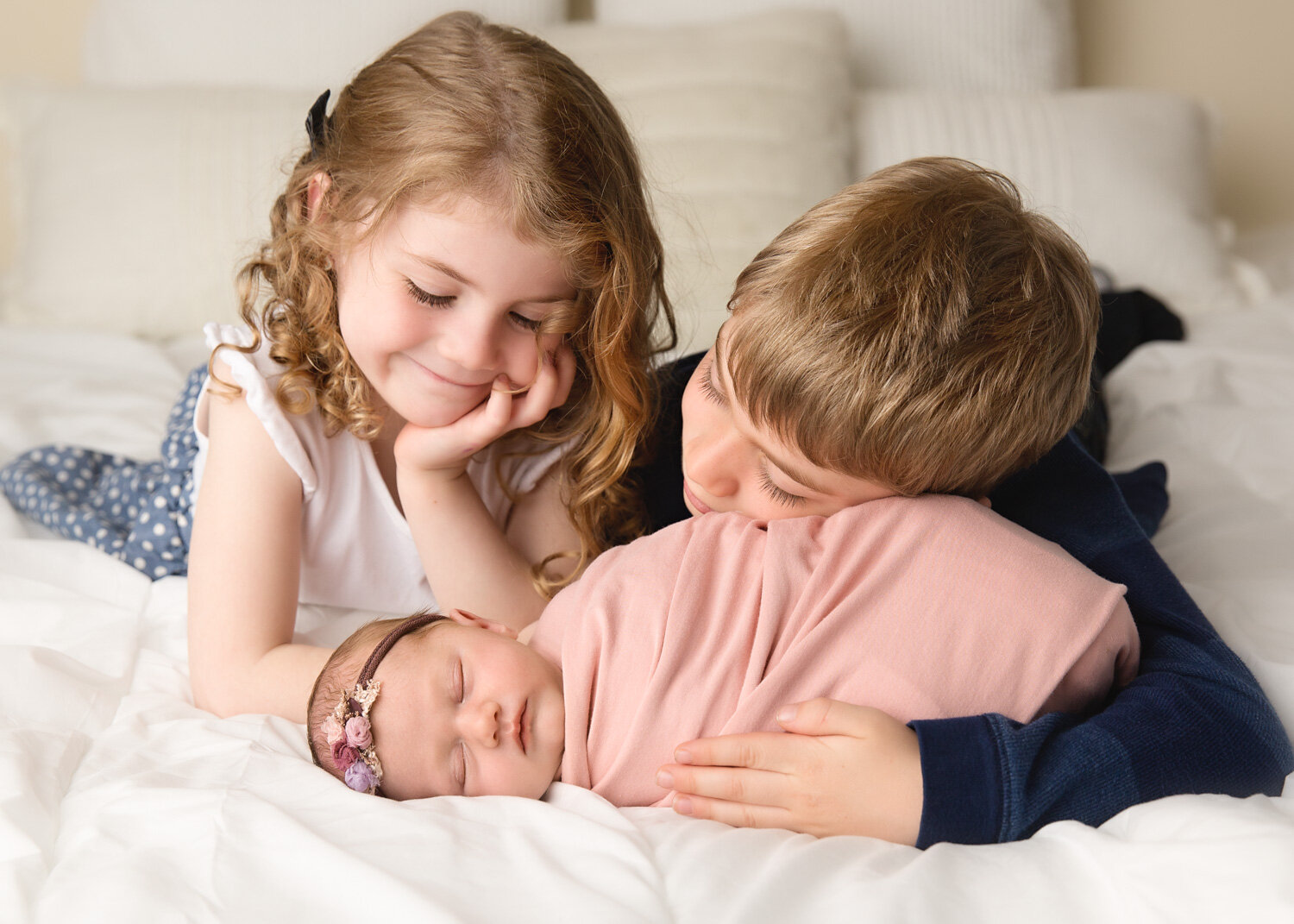  Older brother and sister lovingly look down at new baby sister wrapped in pink in Winnipeg newborn photography studio 