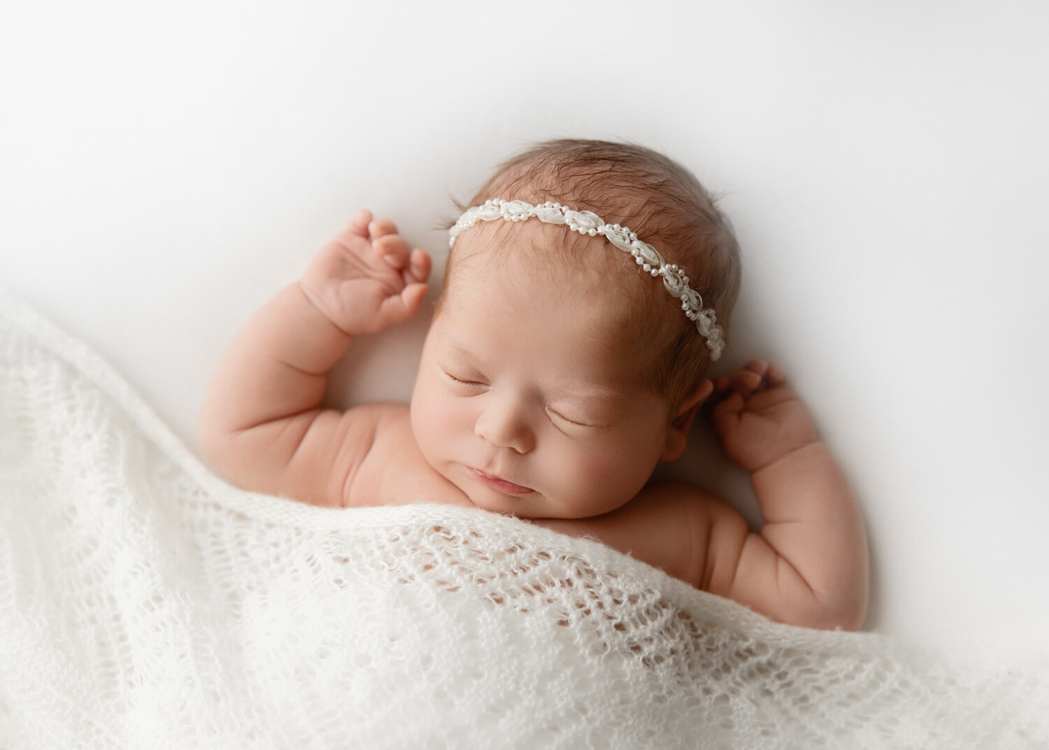  Chubby cheeked newborn baby girl lying on back covered with white lace blanket in Winnipeg newborn studio 