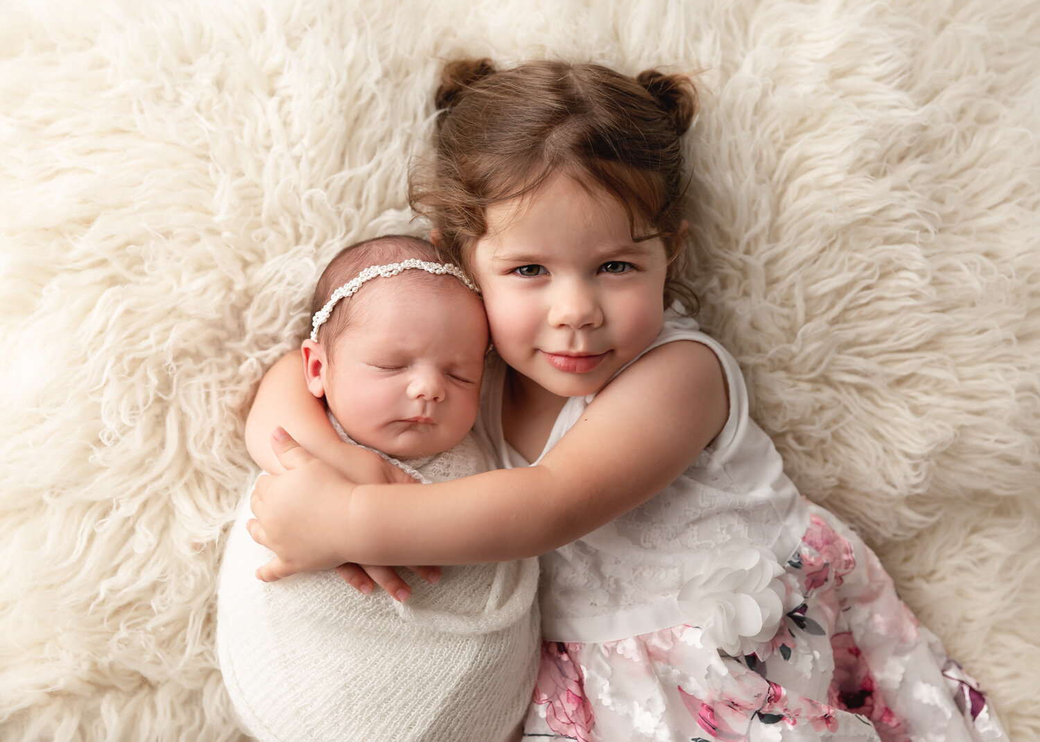  proud older sister cuddles newborn baby dressed in cream and pink for newborn photography photoshoot in Winnipeg 