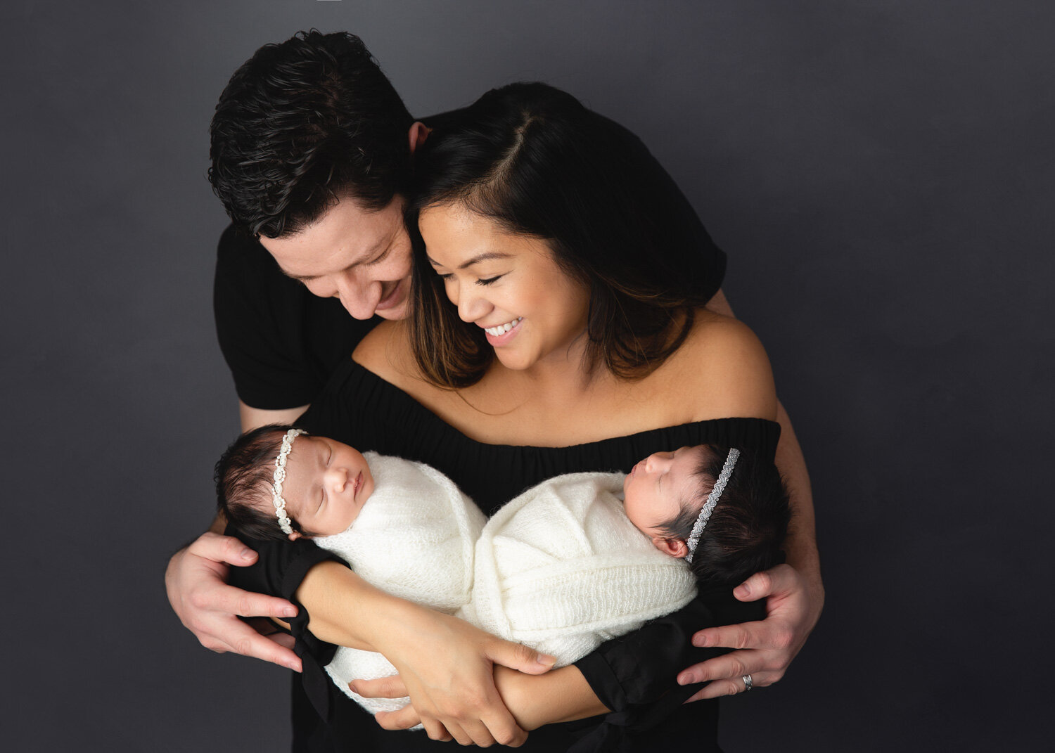  Proud parents looking down at newborn baby daughters in mothers arm during baby photography session in Winnipeg 