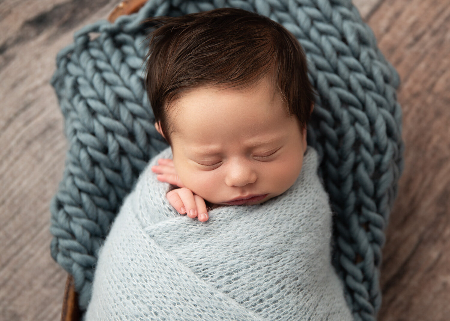  Baby boy in blue wrap and matching wool stuffer hands peeking out sleeping during newborn photography session in Winnipeg 