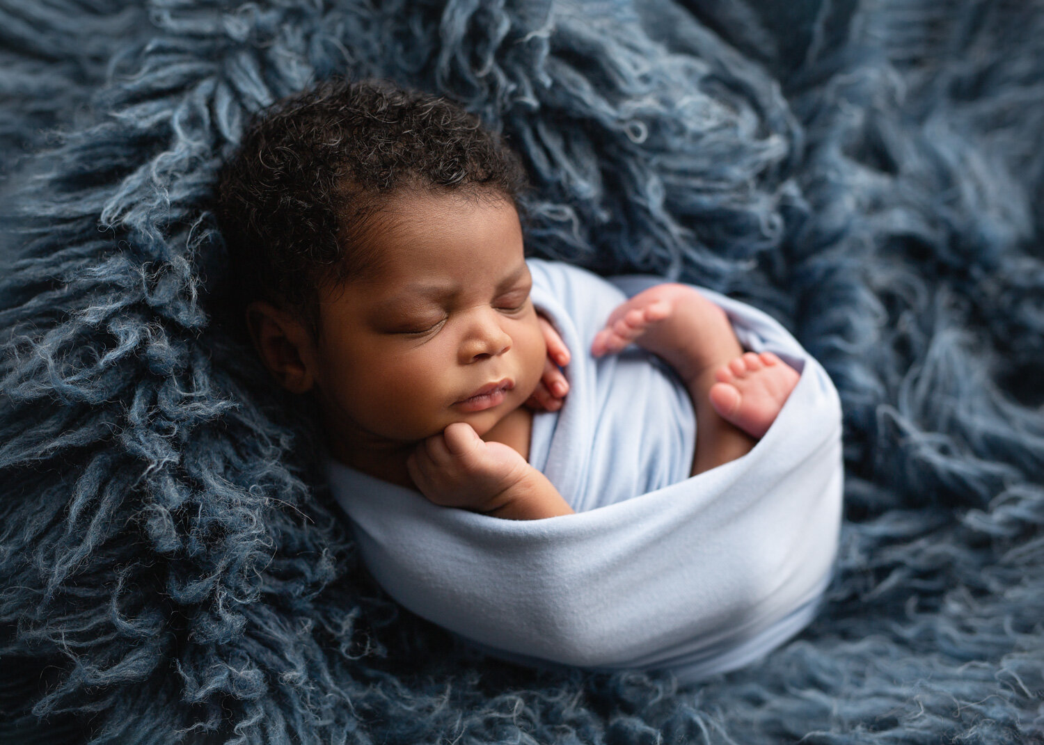  Handsome baby boy wrapped in blue on flokati rug in Winnipeg newborn photography studio 