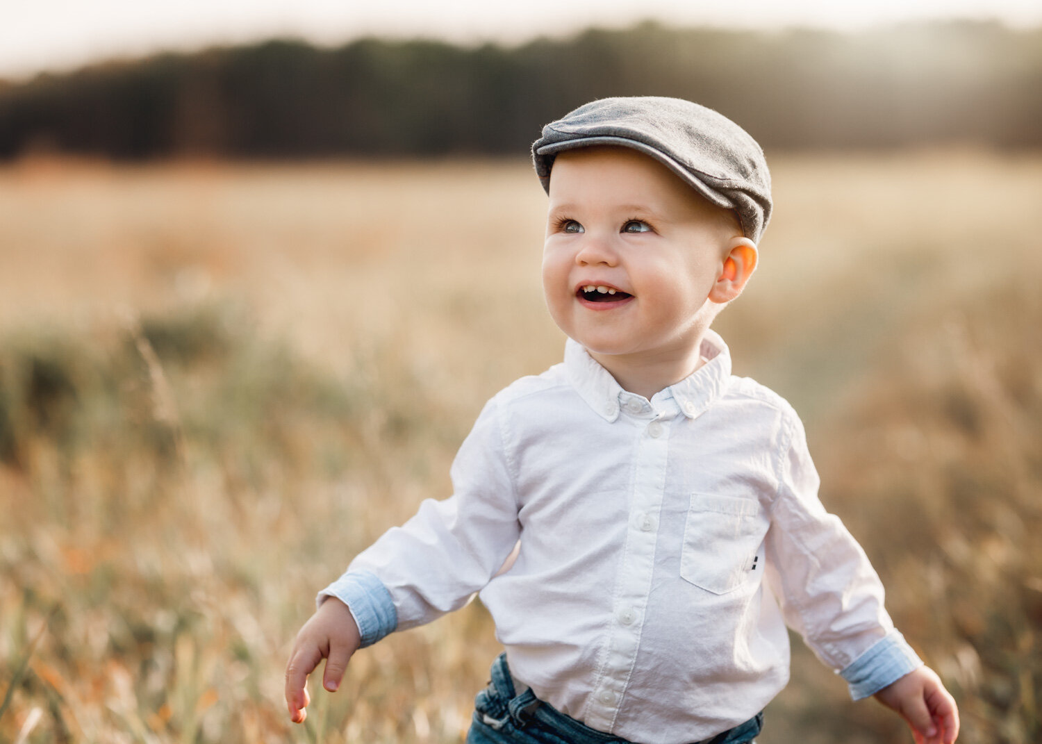  One year old boy in old man's hat walking in prairie grass in Assinboine Forest in Winnipeg 