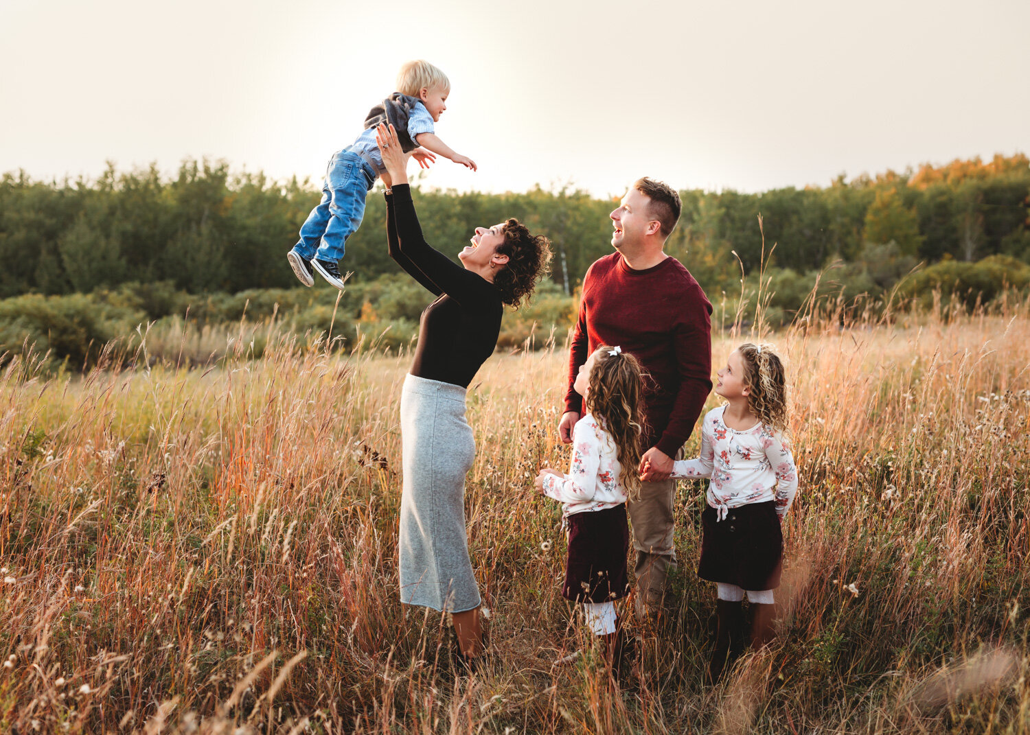  Mother playing airplane with young son and daughters watching in love during family photoshoot Winnipeg 