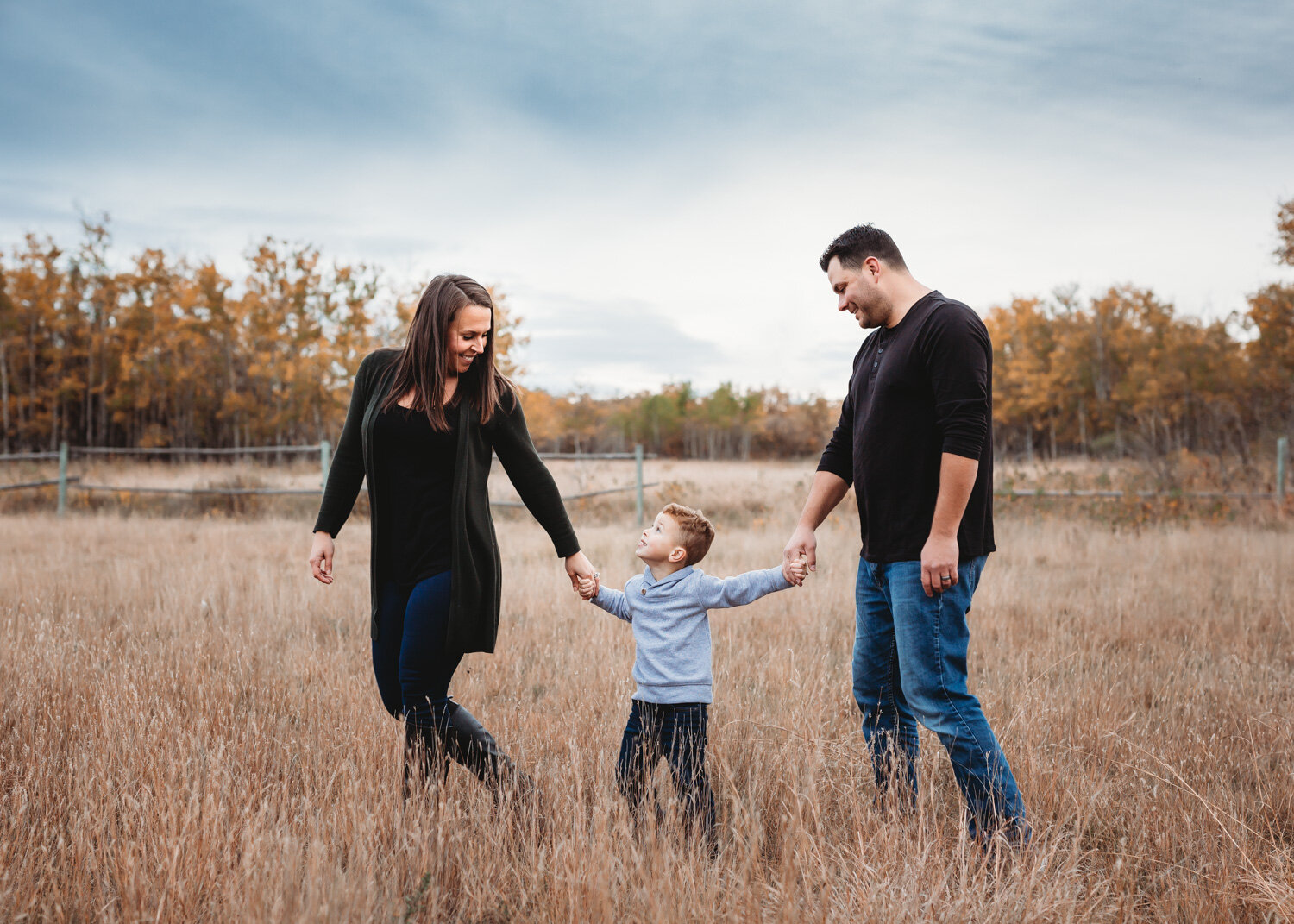  Mom leading young son by the hand with dad in tall fall prairie grass near Winnipeg 