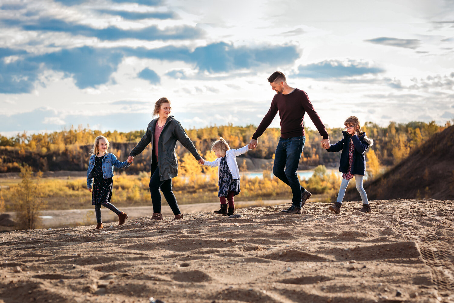  Family of five all holding hand in line walking across sandunes in fall near Winnipeg 