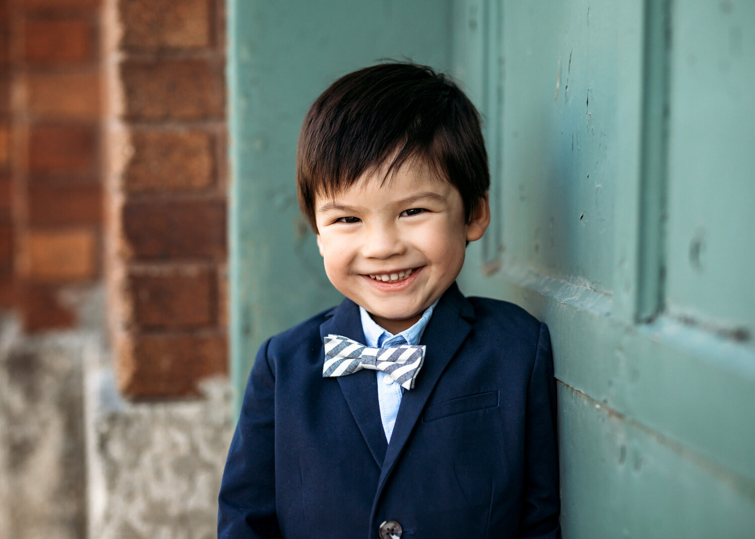  Cutest young boy with striped bowtie in urban setting smiling for photo in Winnipeg 