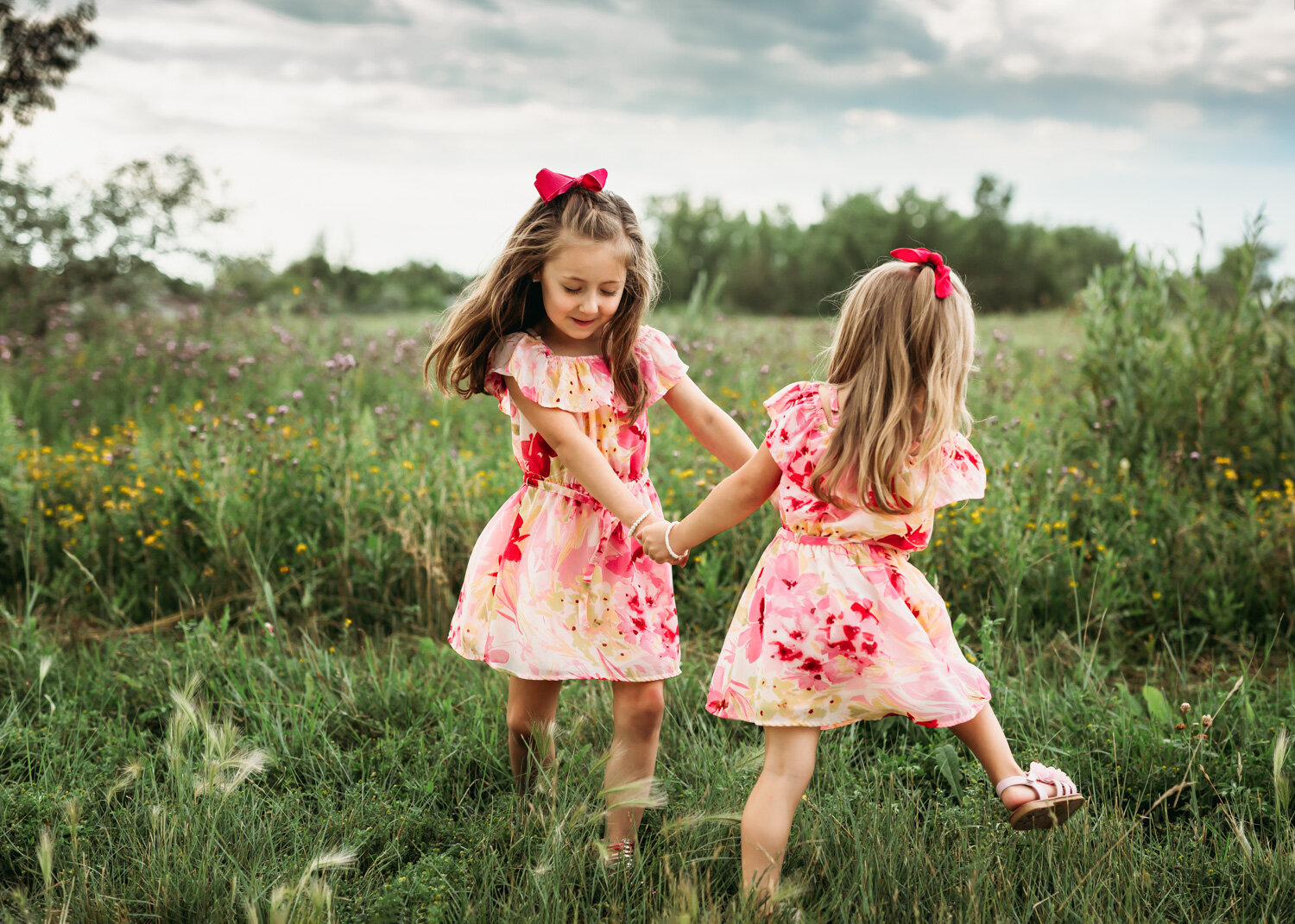  two young sisters playing ring around rosie in grass and flowers in summer in Winnipeg park 