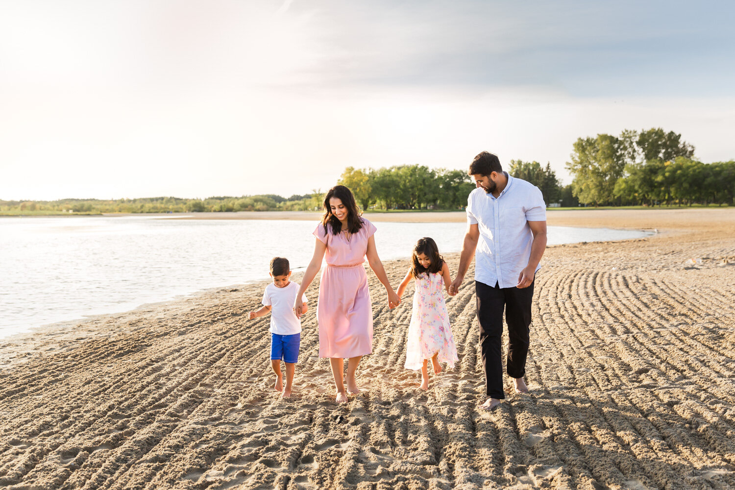  Young family holding hands walking along beach shoreline happy near Winnipeg 