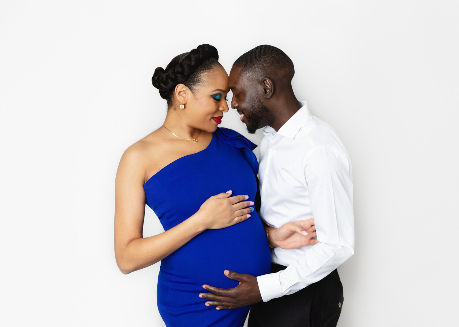  Husband lovingly embracing wife's pregnant belly in royal blue gown during maternity photosession in Winnipeg Studio 