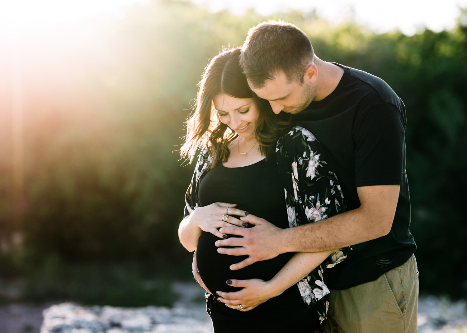  Couple smiling embracing woman's pregnant belly during maternity photoshoot at sunset near Winnipeg 