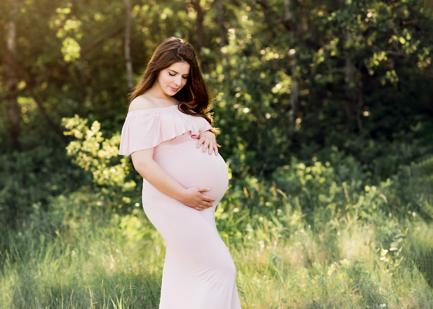  Radiant pregnant mother in pale pink maternity gown hoding belling in spring field near Winnipeg 