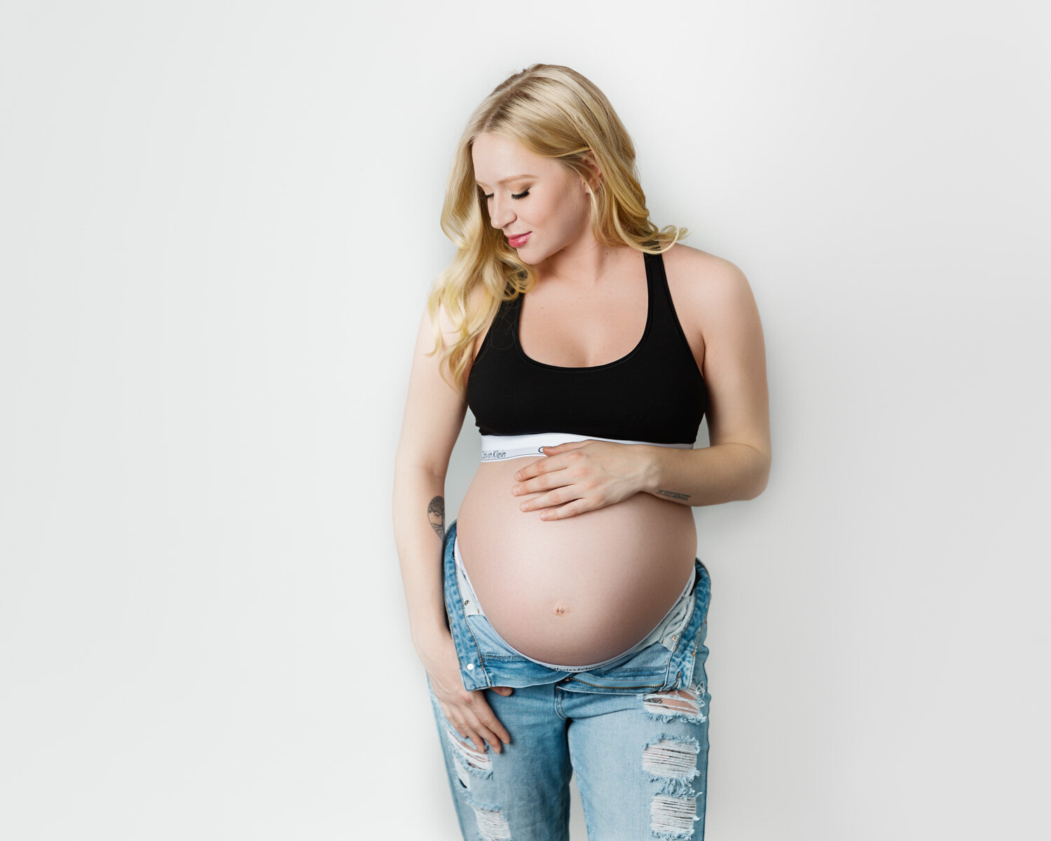  Pregnant woman in Calvin Klein bra top and jeans with pregnant belly in Winnipeg maternity studio 