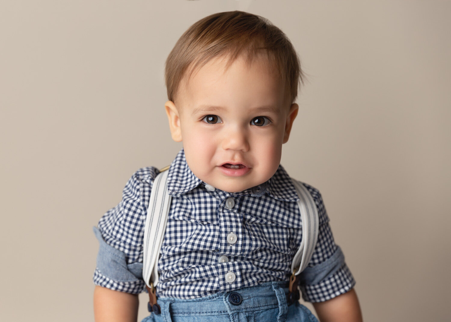  One year old with big brown eyes and grey suspenders sits for portrait in Winnipeg photography studio 