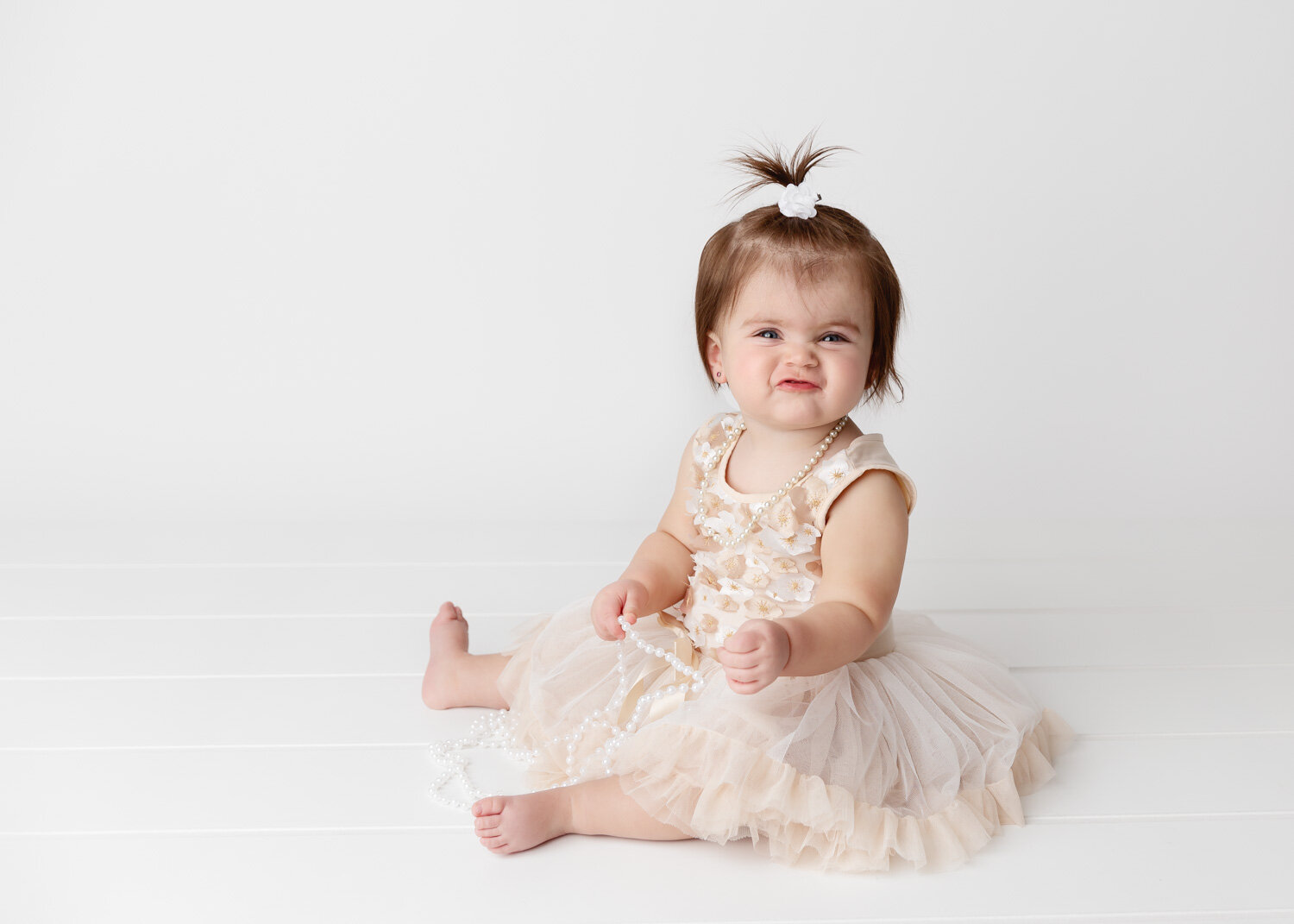  Sassy cute one year old girl in gold dress holding white pearls for child photography session in Winnipeg 