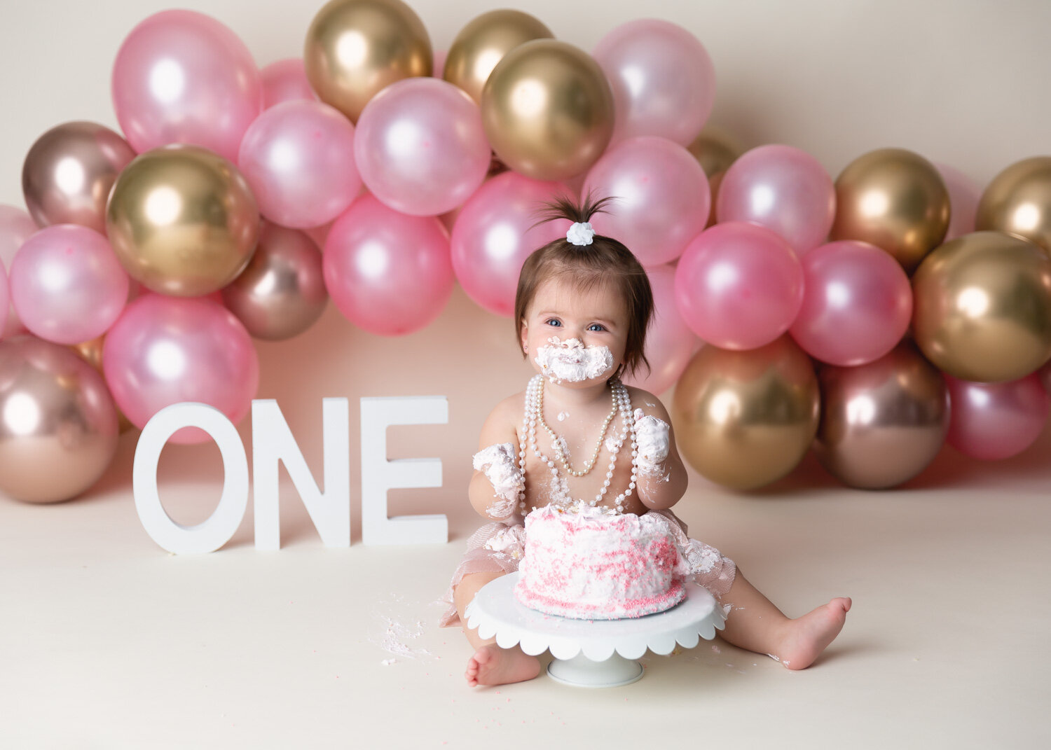 Adorable girl with white pearls sporting messy cake face and hands during cake smash photography session in Winnipeg 