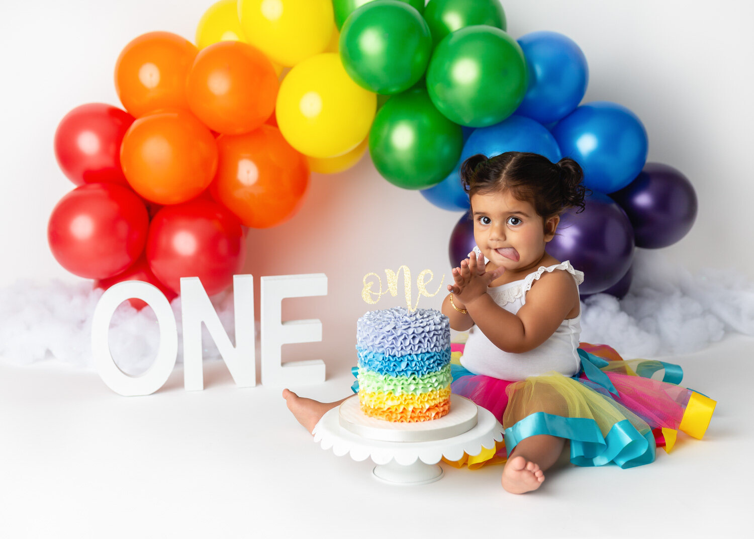  Girl in bright rainbow tutu waiting with tongue out to start cake smash for photography session in Winnipeg 