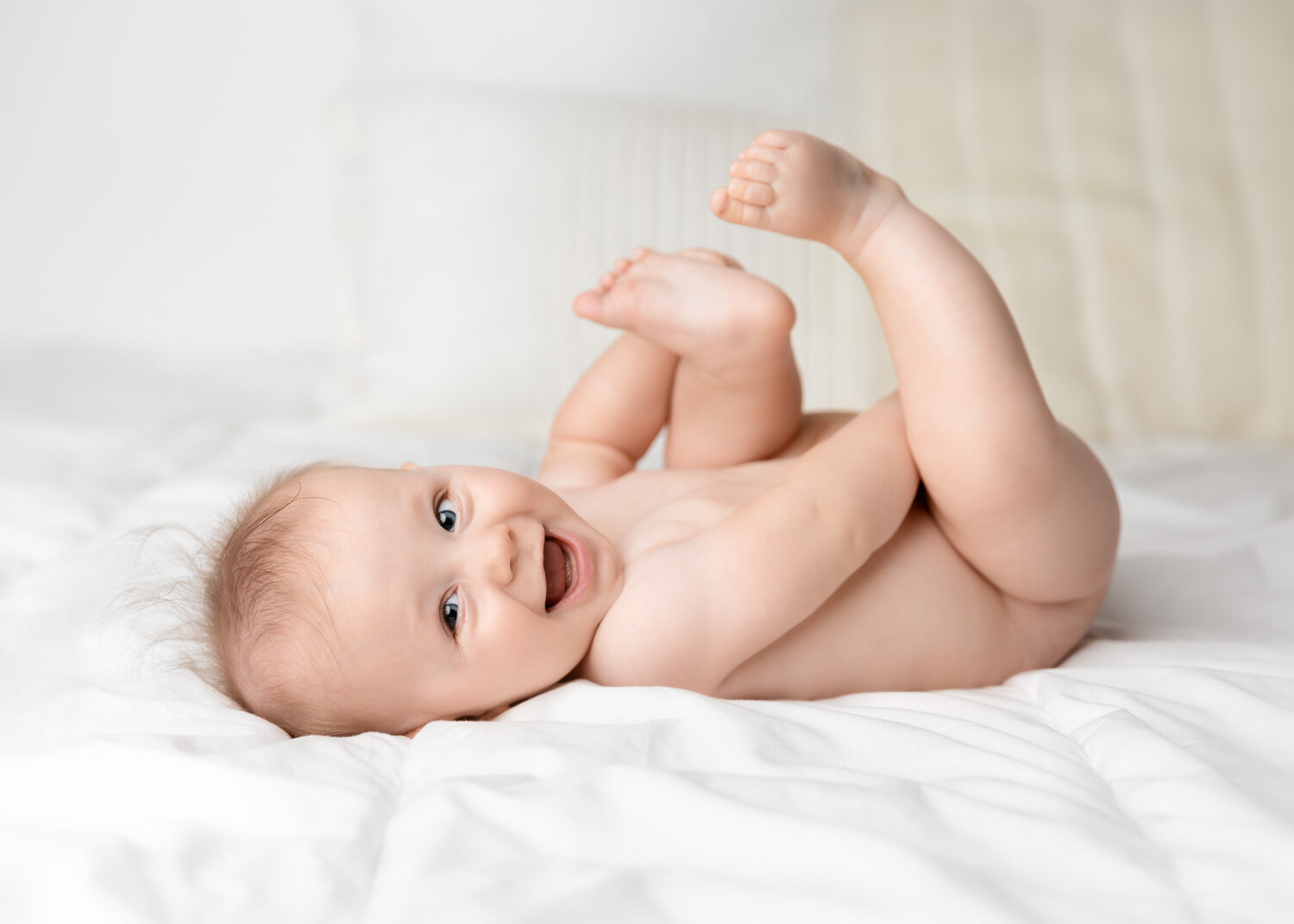  Baby smiling holding toes on white duvet during child photoshoot Winnipeg 