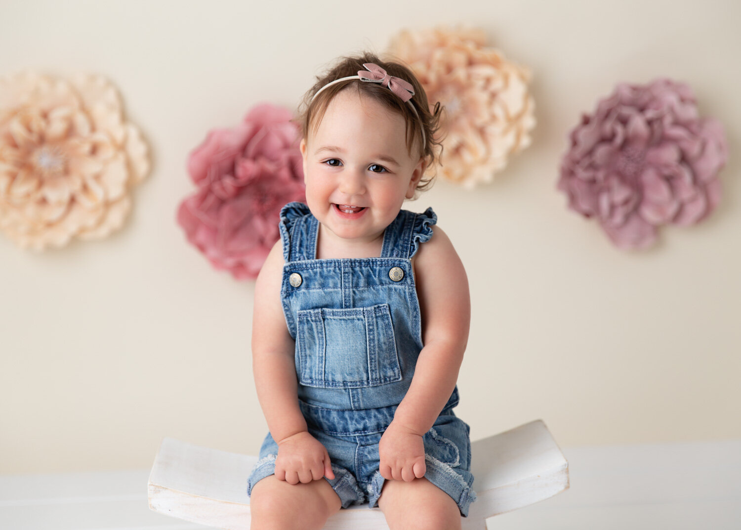  Sweet girl in denim overalls and rose floral background smiling for milestone photography session in Winnipeg 