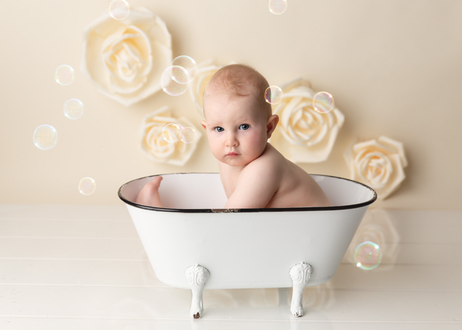  One year old with big blue eyes splashing in white antique tub after cake smash photography session in Winnipeg 