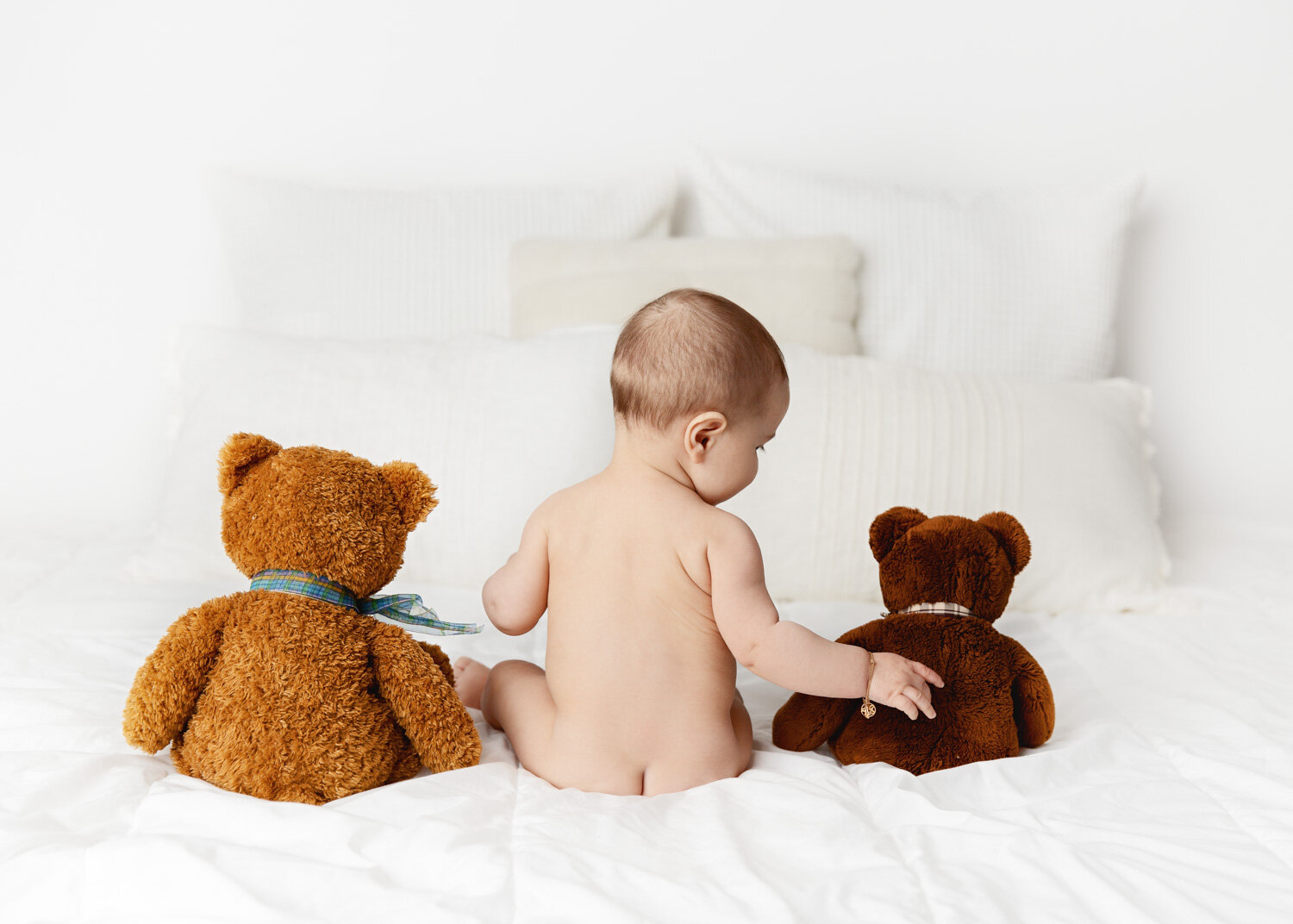  Bare bumb baby boy sitting with two brown teddy bears on white duvet in Winnipeg for sitter photography session 