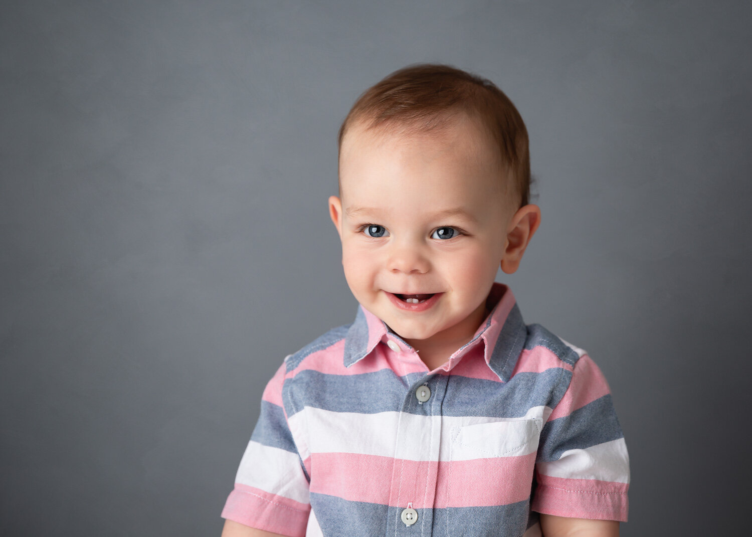  Young boy in white grey and pink dress shirt smiles during photoshoot in Winnipeg studio 