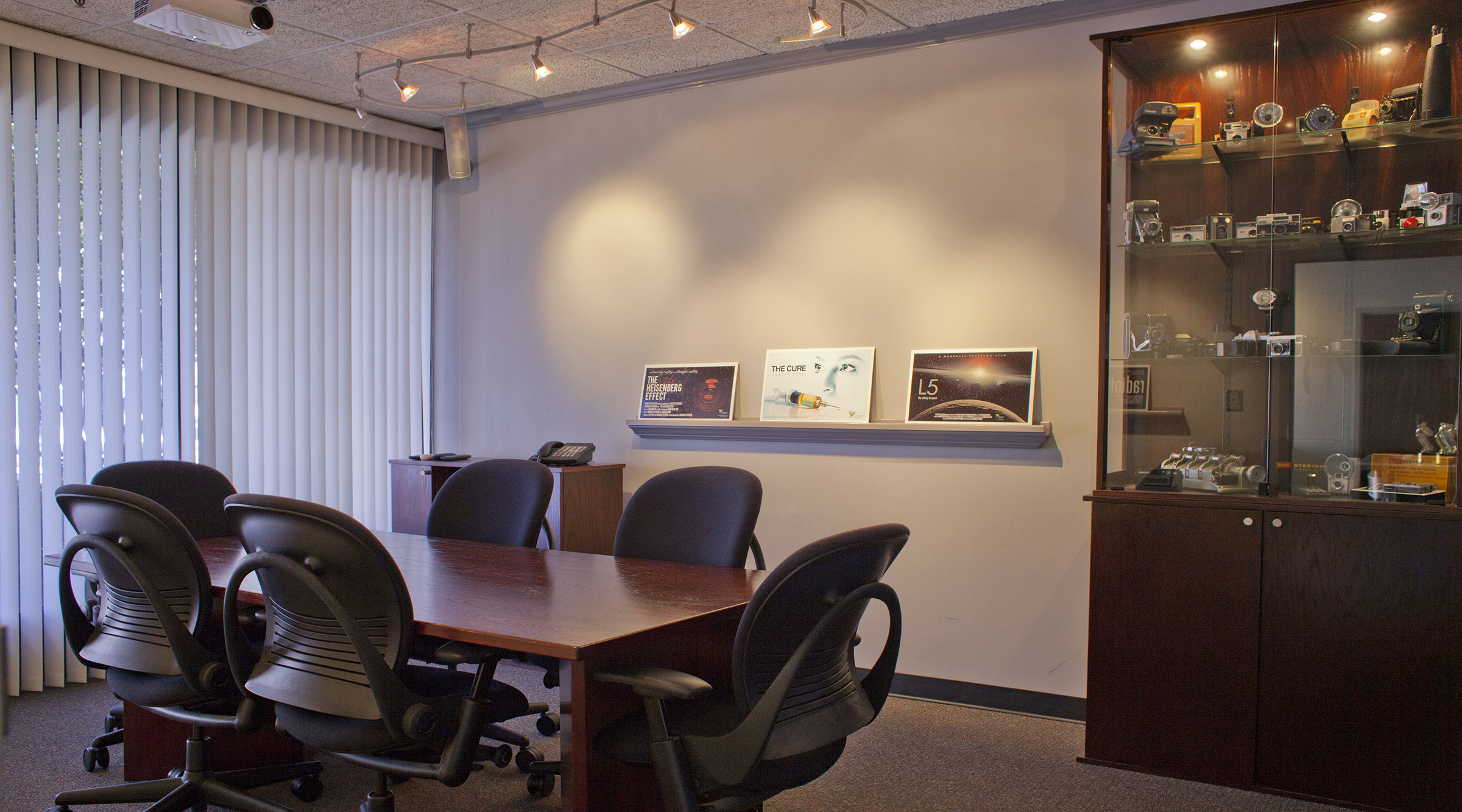 This is our conference room. It has a table, indirect lighting, some comfortable Steelcase Leap chairs, a museum of unusual and vintage cameras, HD projection to a 90” screen and big windows that look out to the parking lot. We also have skinny shelves to display storyboards. It’s a conference room.