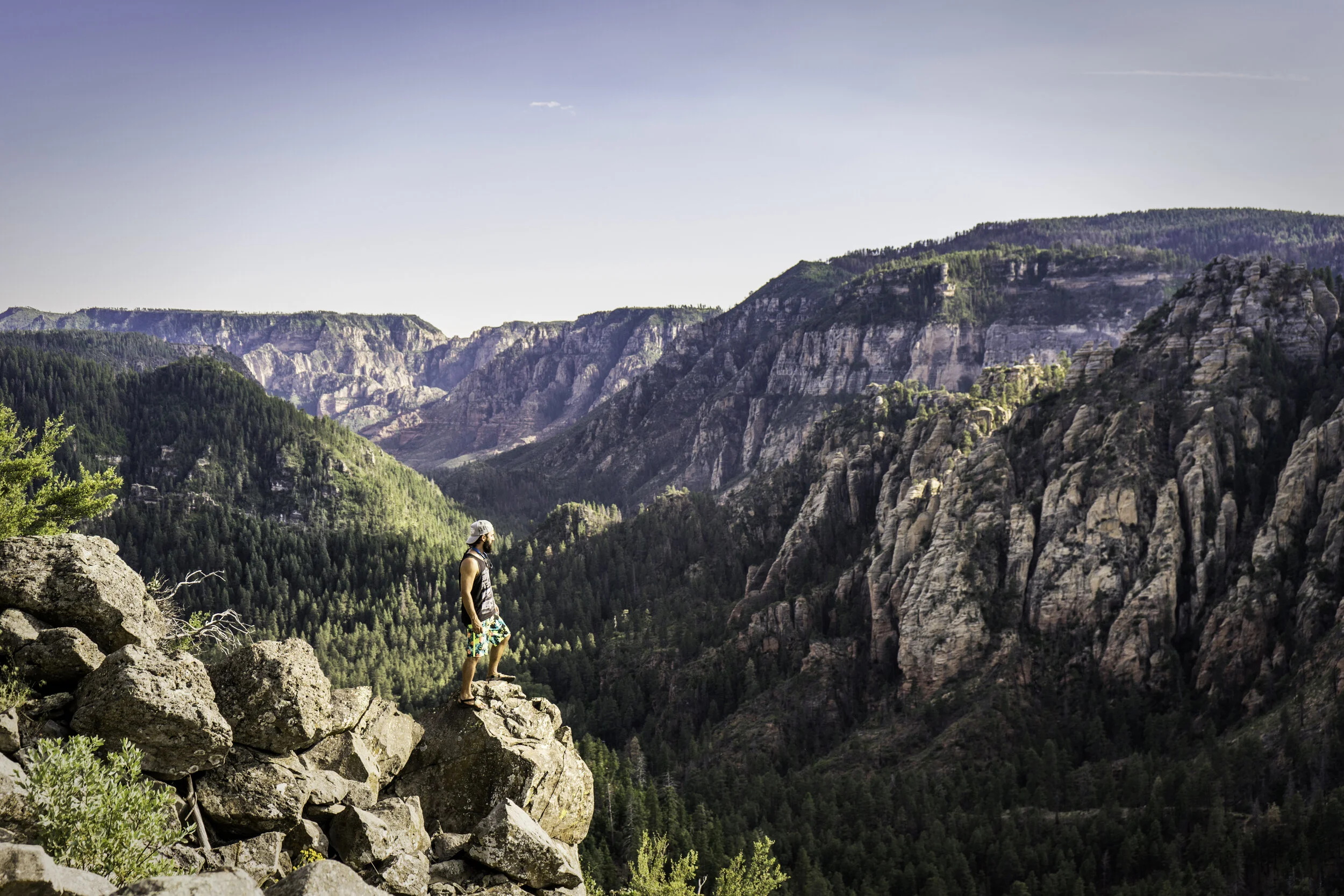 Guy standing on a cliff edge overlooking Oak Creek Canyon after hiking up Cookstove Trial in Sedona