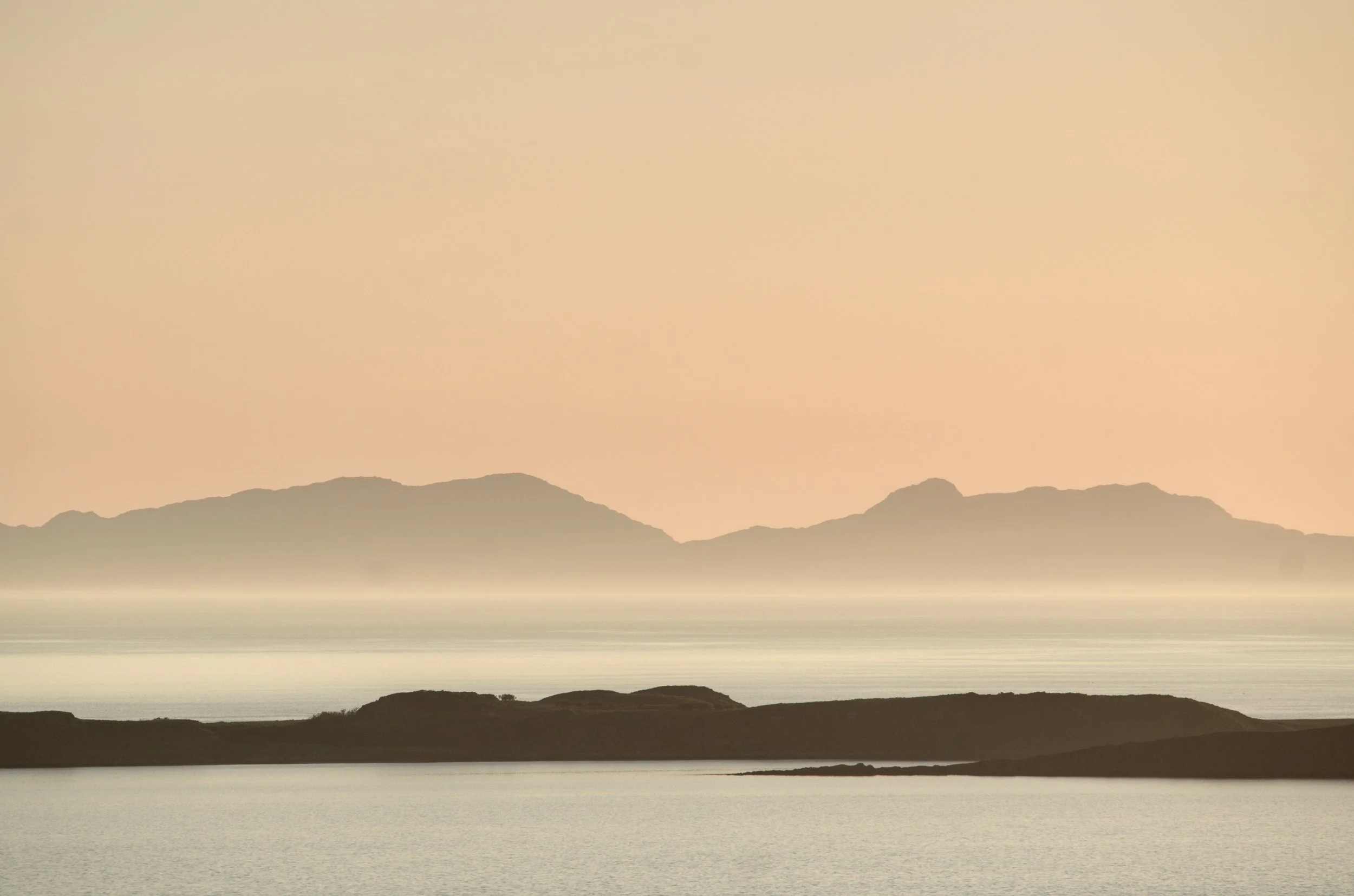 Waternish Sunset. The view westwards from the Waternish peninsula on the Isle of Skye in Scotland, as the sunlight colours the sky with soft hues that help define the simple shapes of the landscape against the sea.