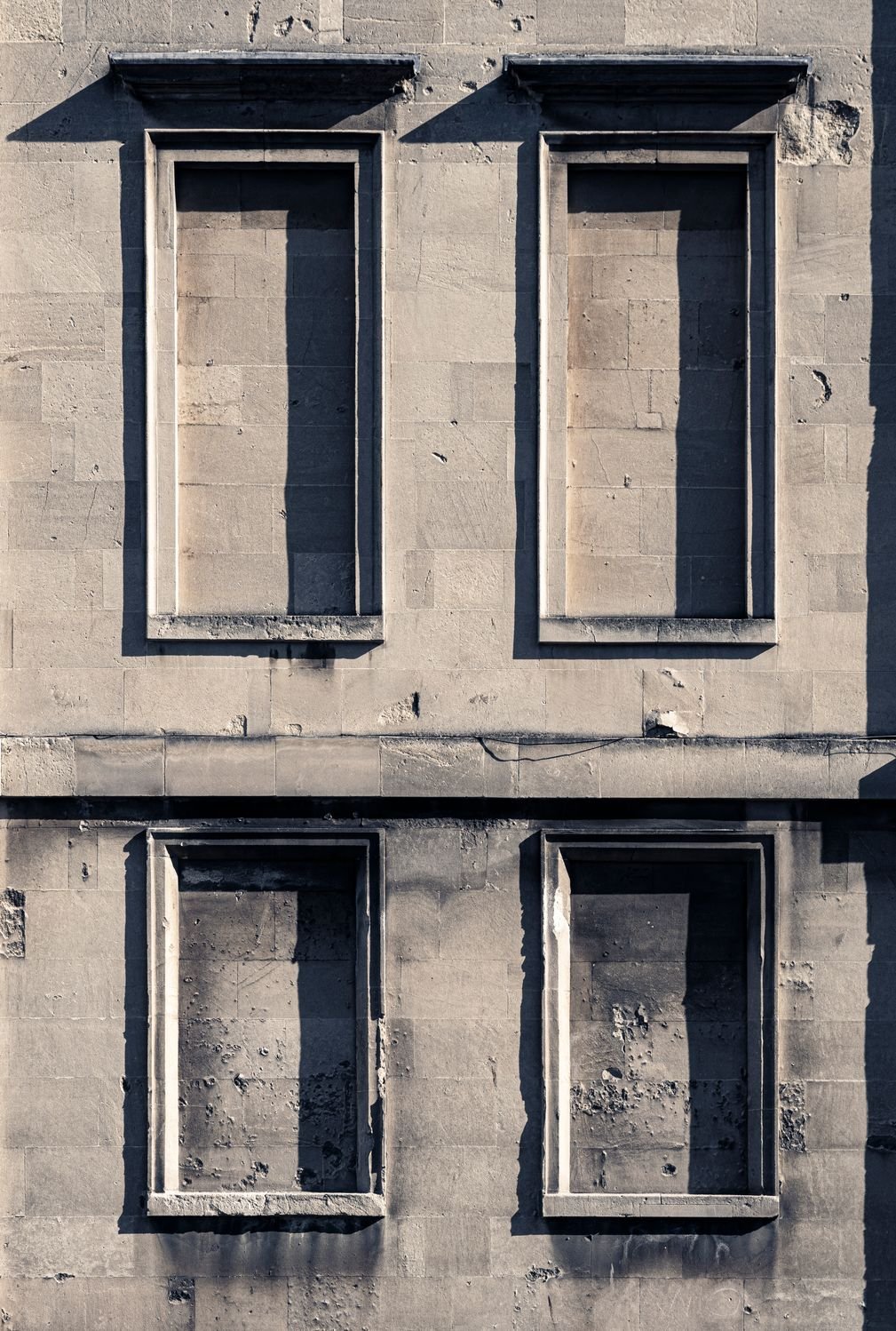 Four 'blind' windows in stone, on a building in Bath, England. Heavily side-lit by strong sunshine casting deep shadows.