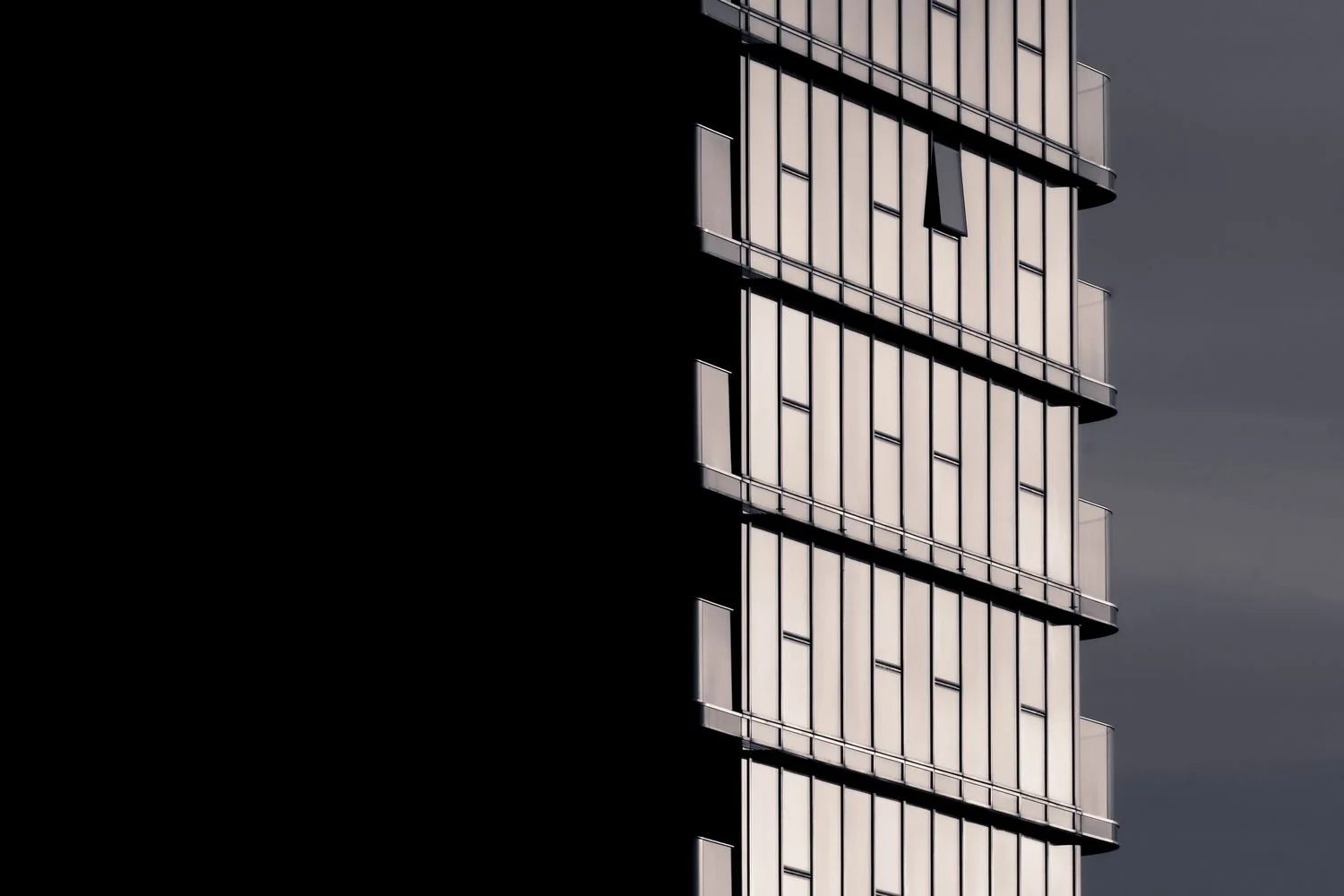 Graphic photo of residential tower at Chelsea Waterfront, London. One side is deep in shadow, the other lit by the sun as the reflections and window frames make a grid.