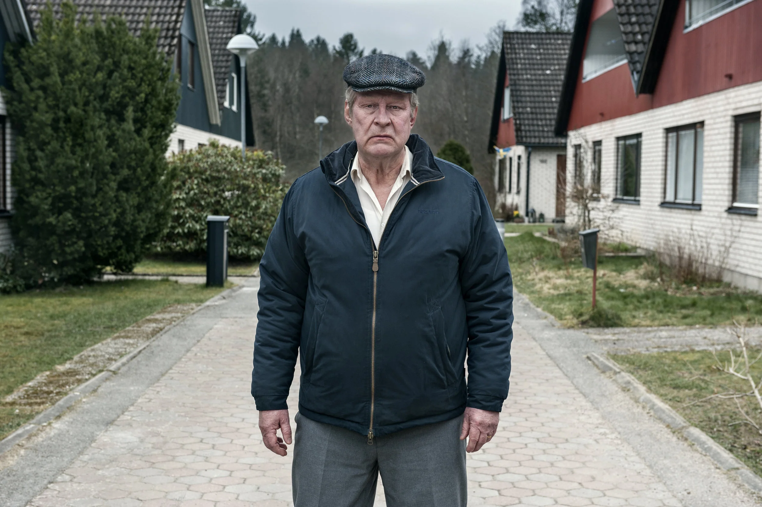 A bitter Ove (Rolf Lassgård) stands in the middle of the gated community pathway where cars are prohibited. 