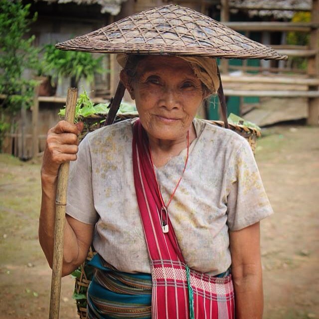 82 and still carrying baskets the same weight as a 20 year old. 
Under her hat you can just see a leather strap wrapped around her forehead to secure the heavy load. She is taking her basket load of greenery to the local makeshift store in the camp h