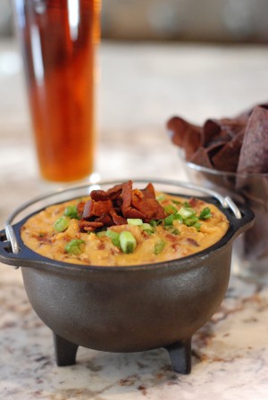 This Ale, Bacon and Cheddar dip was inspired by my mother’s home state of Wisconsin, and the football team that I love. It’s perfect for entertaining on any given Sunday with family or friends. The dip is best served hot, and I recommend using a fondue pot or small cast iron caldron. Lodge makes the little cast iron caldron I used in the picture above. I love it because it stays hot for a long time without a heating element, which is perfect when children are around. The company was founded in Tennessee over 100 years ago and they’re still making the best skillets, Dutch ovens and griddles you can buy. Serve this dip with tortilla or pretzel chips. Active Time: 30 minutes Makes about 4 cups Ingredients 1½ lb thick cut applewood smoked bacon 2 cups sweet onion, diced 1 tablespoon garlic, diced 2 tablespoons flour 1 bottle amber ale – I like to use Boont Amber Ale from Anderson Valley Brewing Co. ½ cup whole milk 4 oz cream cheese, softened 4 oz finely shredded (about 2 ½ cups) sharp cheddar 4 oz finely shredded (about 2 ½ cups) aged extra sharp cheddar 1 scallion, light and dark green parts only, finely chopped Preparation Cut bacon into ¼-inch strips. Heat a large skillet over medium-high heat and cook the bacon until crispy, 4 to 6 minutes. Transfer the bacon to a paper towel lined plate. Pour off all but 2 tablespoons of the bacon fat from the skillet. Turn the heat to medium and add the onions. Sauté until onions are soft and translucent, about 5 minutes. Add the garlic and cook for another minute or two. Sprinkle the flour over the onions and cook, stirring, until flour has coated onions and is lightly golden brown, 1 to 2 minutes. Add one bottle of ale slowly, whisking as you pour to avoid lumps. Cook until mixture has thickened, 3 to 4 minutes. Add the milk, and then cream cheese, whisking until smooth after each addition. Turn the heat to low and fold in the shredded cheese, stirring until melted. Gently fold in bacon, reserving about ¼ cup for garnish. Transfer the dip to a small fondue pot or little cast iron cauldron. Top with remaining bacon and chopped scallions. Serve with tortilla or pretzel chips.
