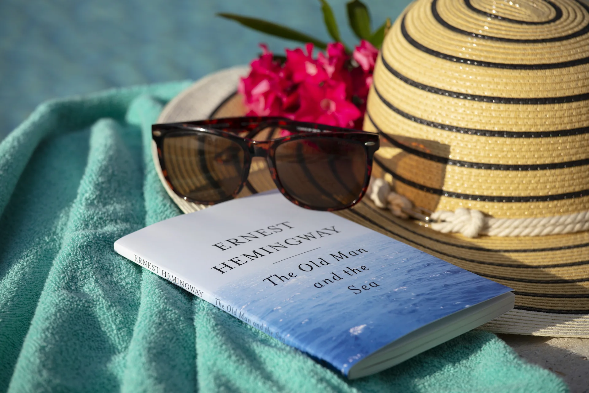 Image of sunglasses, book, and sun hat on pool towel
