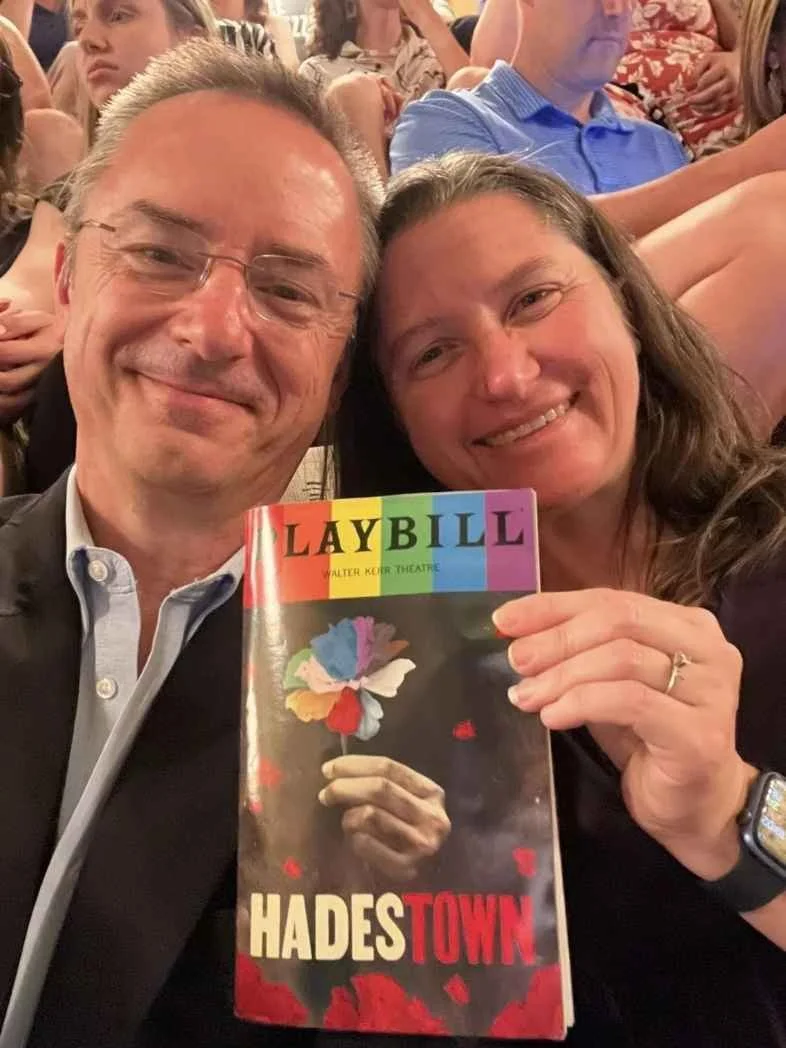 Chuck and Renee Taft at a theater, holding a playbill for "Hades Town." They are sitting in a packed theater.
