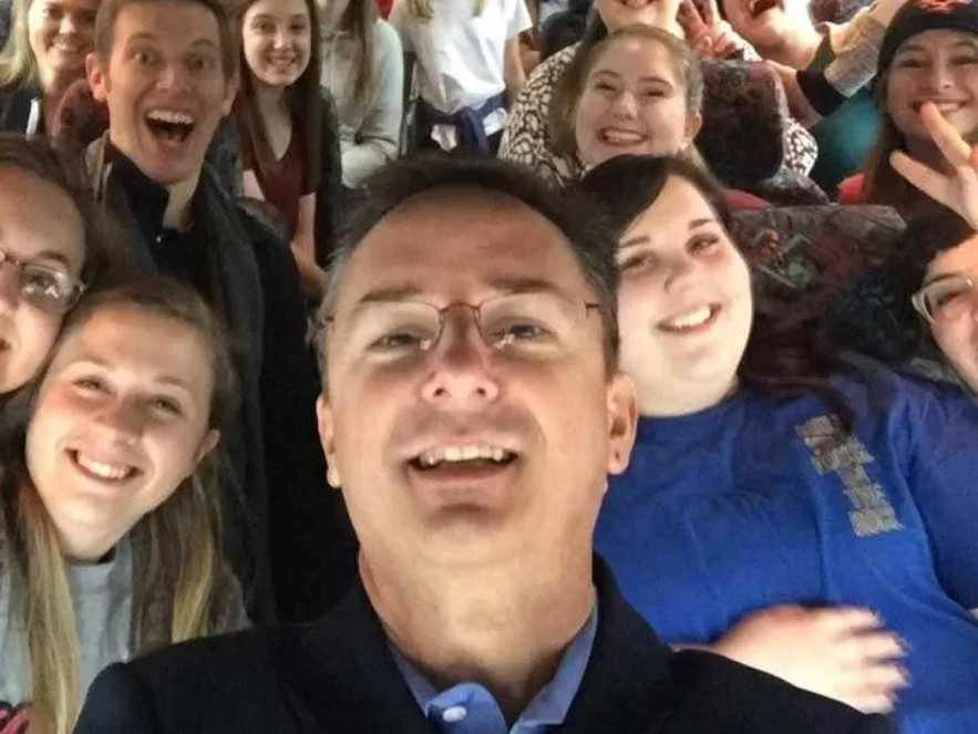 Group of young students and a man taking a selfie on a bus, smiling and having fun.