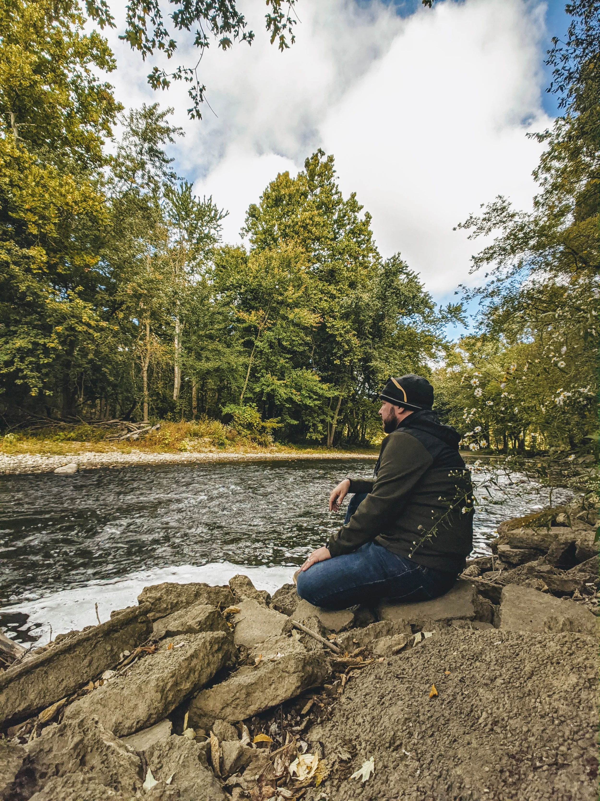 Adam Bouse, certified forest therapy guide and author, sitting along the banks of a river