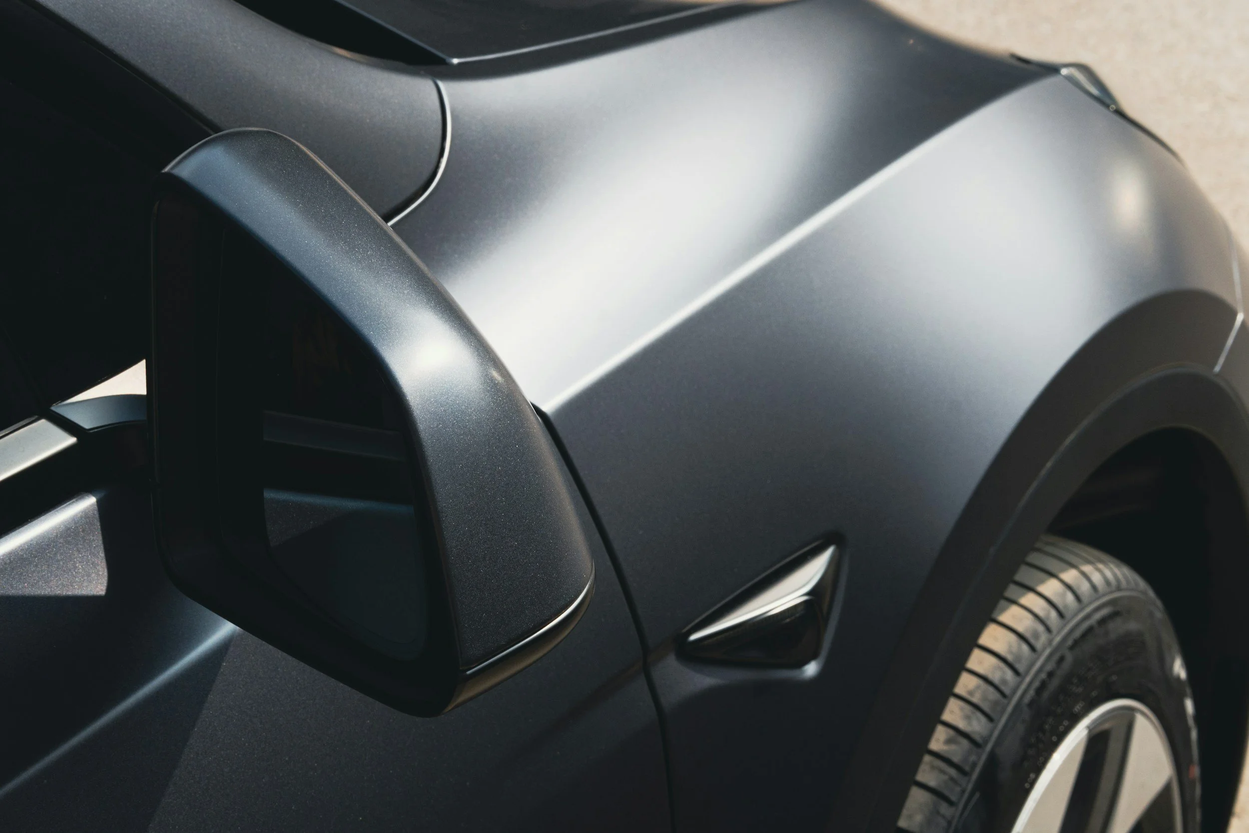 Close-up of a dark gray or black car with a side mirror, wheel, and part of the fender visible.