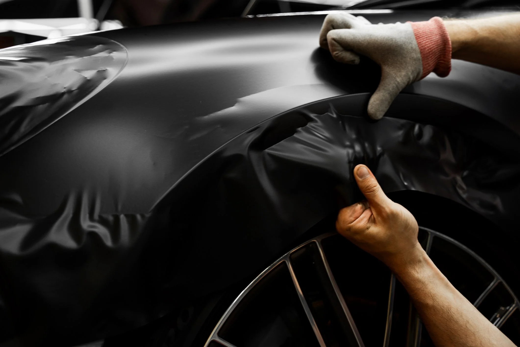 Close-up of a person's hand peeling off protective film from a black car's hood.