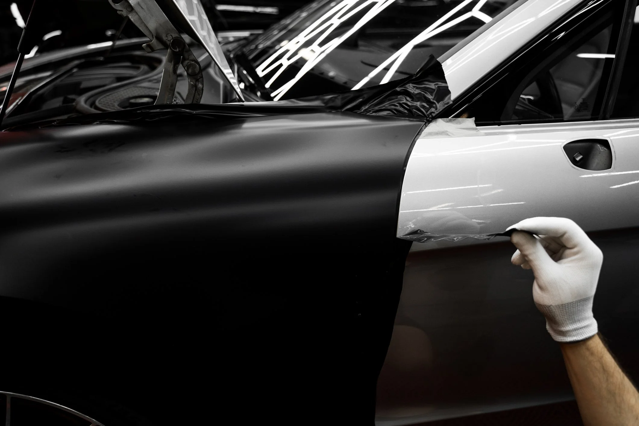 A person wearing a white glove is applying a protective film to the side of a black and white car.