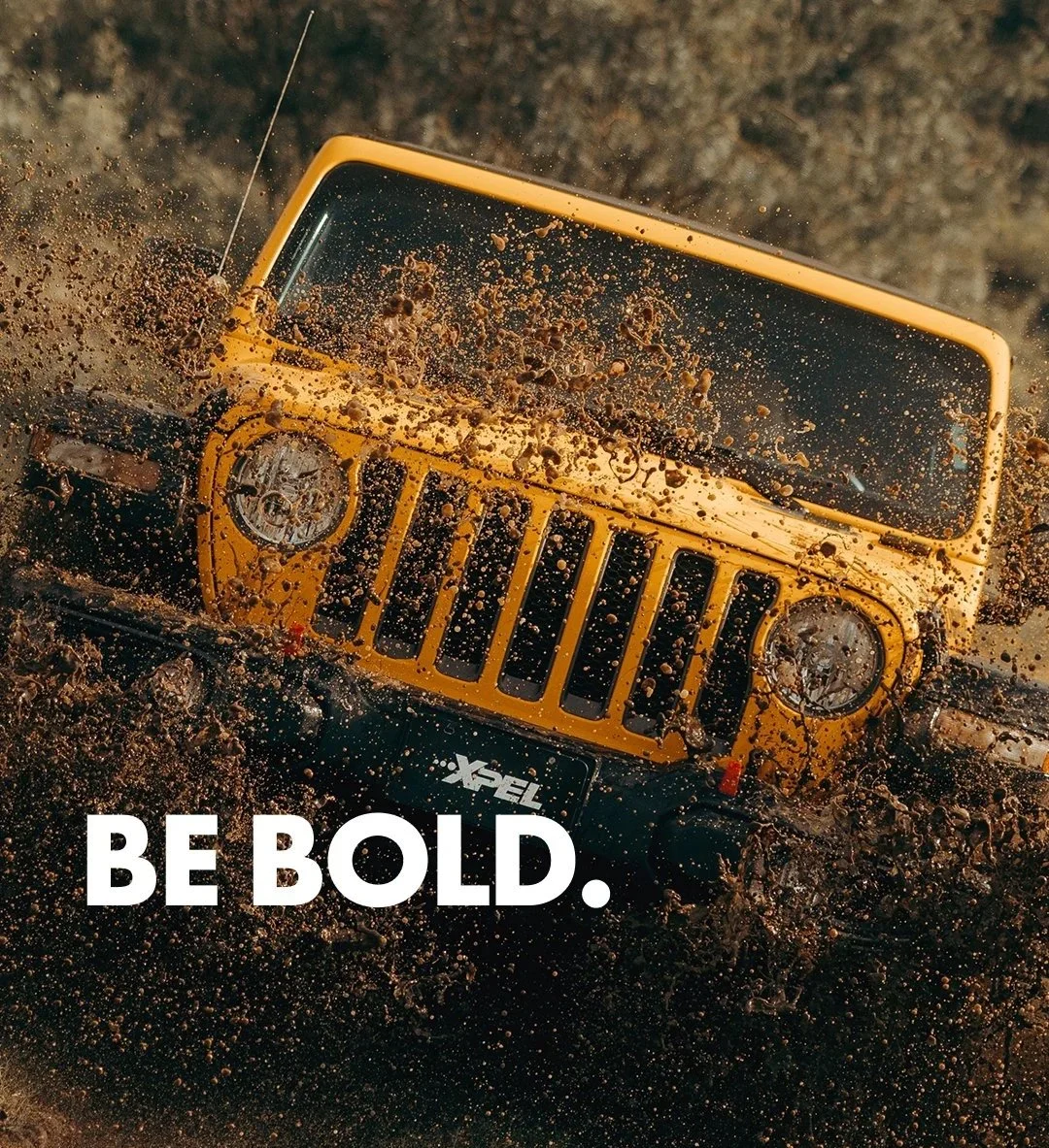 Yellow Jeep driving through muddy terrain with mud splashing around