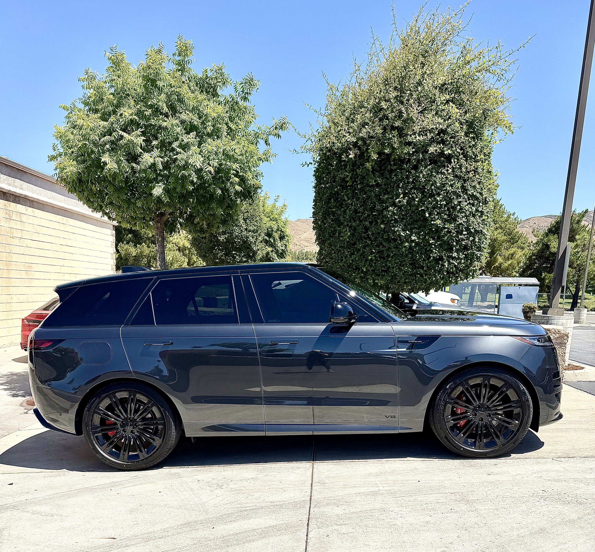 Black electric car parked on the street with three large trees and a bright blue sky in the background.