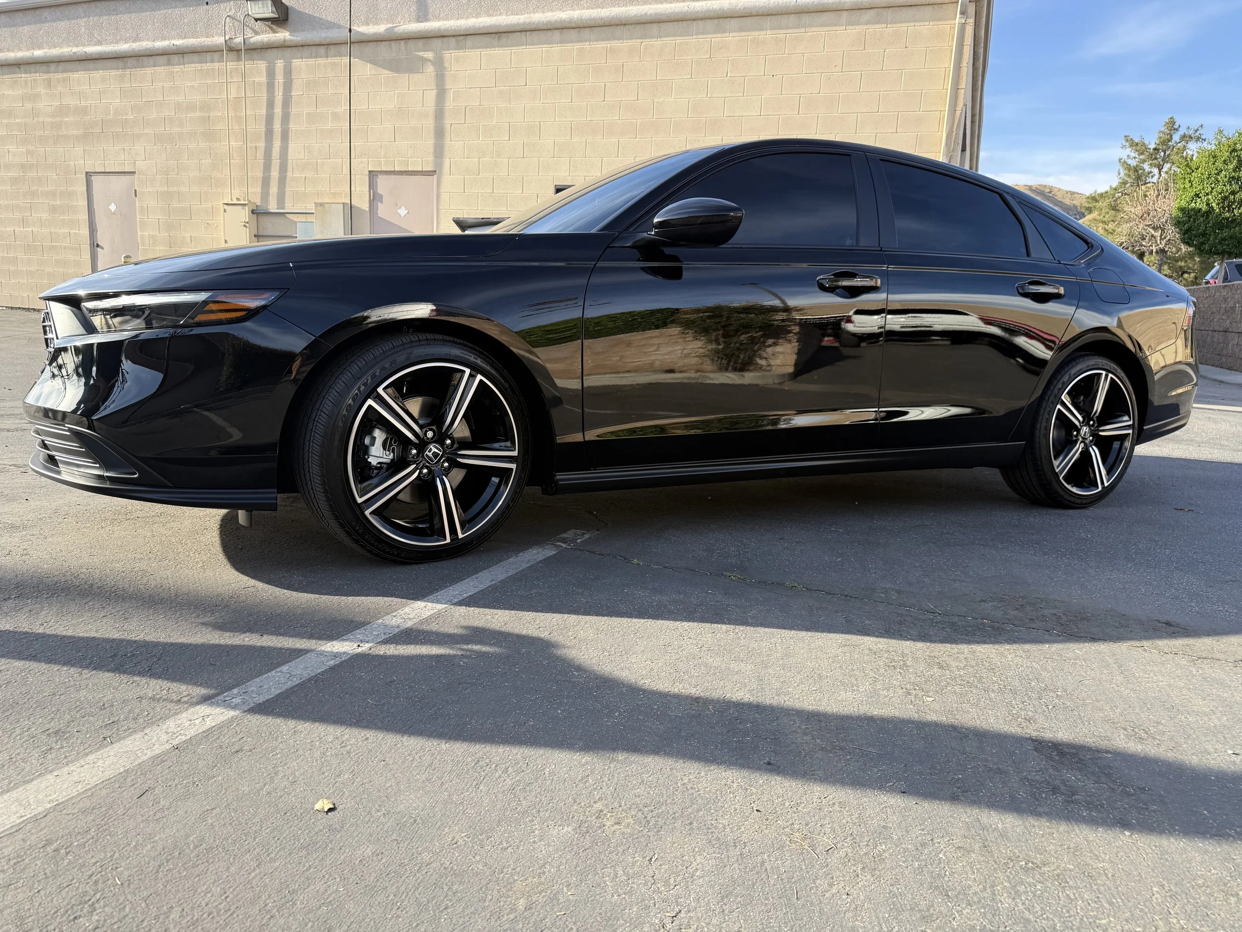 A black sedan cars parked in a parking lot near a beige brick building with trees in the background under a clear blue sky.