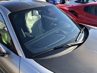 A silver sports car parked next to a red vehicle, with the view focusing on the windshield and part of the dashboard.
