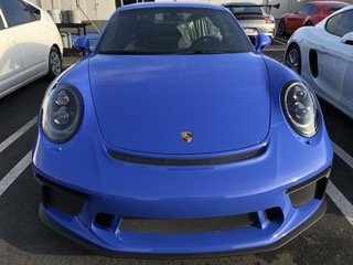Front view of a blue Porsche sports car parked in a parking lot.