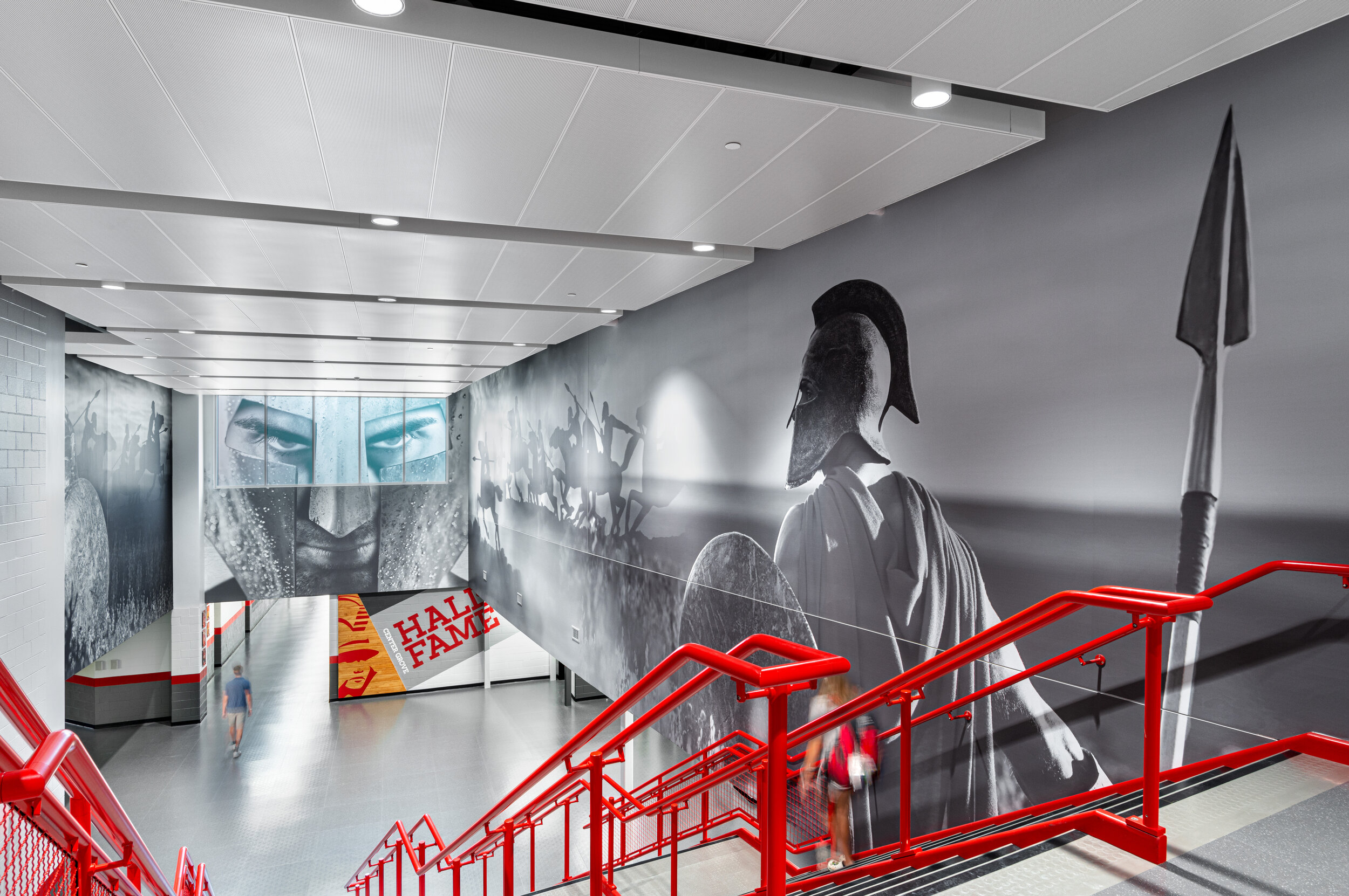 An architectural photography of red handrails and a hall with photos of a Greek warrior.