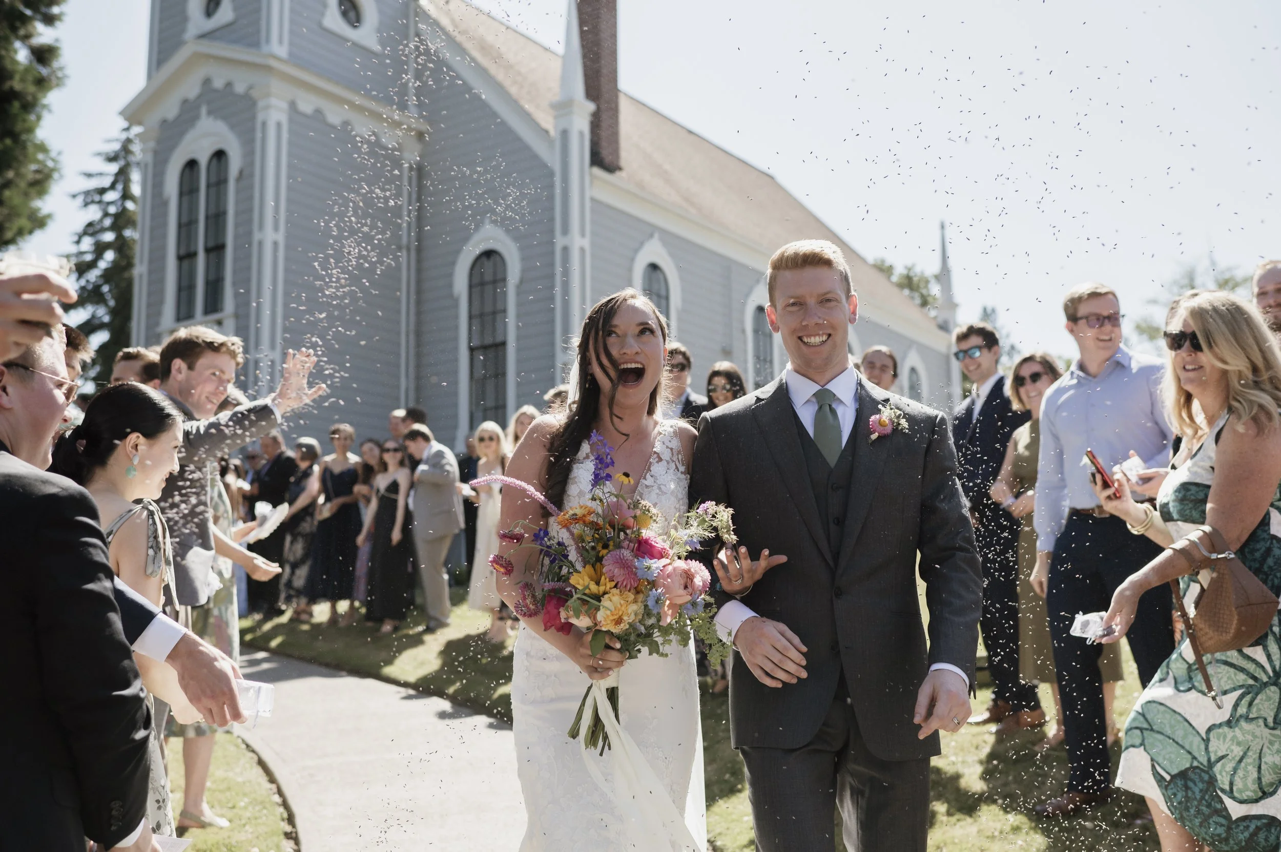 A joyful newlywed couple walking out of a church after their wedding ceremony, surrounded by friends and family throwing confetti and celebrating on a sunny day.