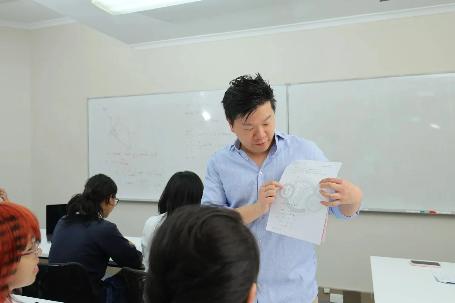 A teacher reviewing a diagram with students in a classroom with a whiteboard in the background.
